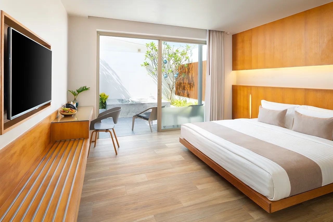 Helles Hotelzimmer mit Holzboden, Doppelbett und Schiebetür zu einer privaten Terrasse.