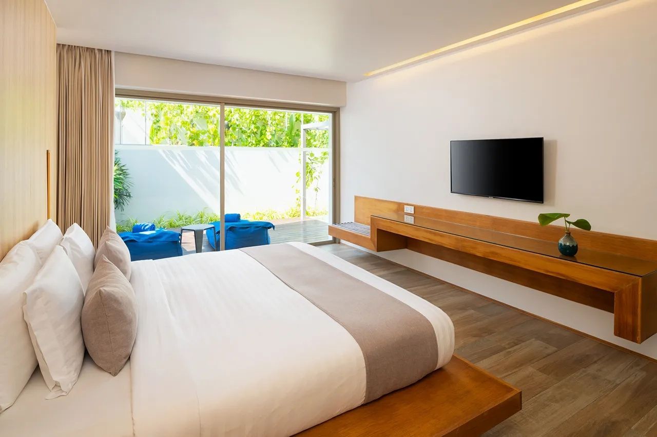Helles Hotelzimmer mit großem Doppelbett, Wandfernseher und Schiebetür zur Terrasse.