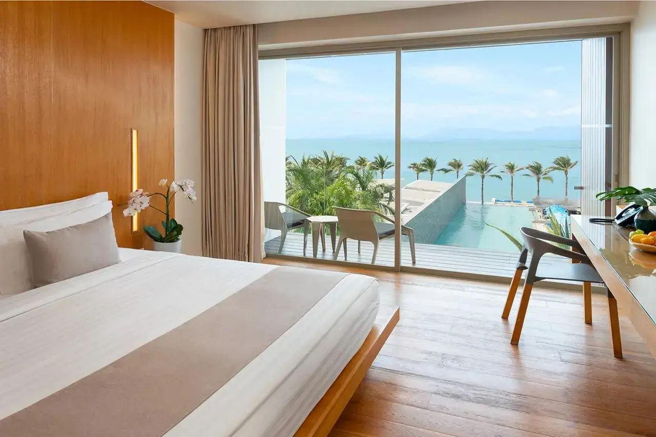 Blick durch ein großes Fenster auf die Terrasse mit Sitzmöglichkeiten, Pool und Meer.