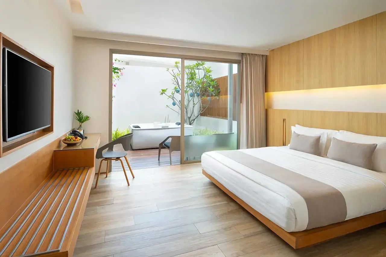 Hotelzimmer mit Parkettboden, Doppelbett und breiter Glastür zur begrünten Terrasse.