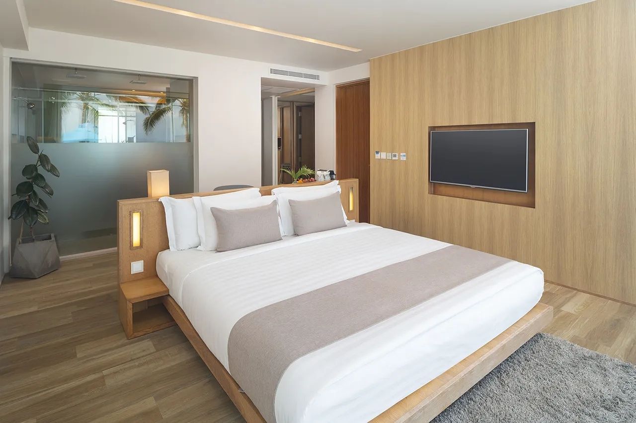 Helles Hotelzimmer mit großem Doppelbett, Holz-Kopfteil und Flachbildfernseher.