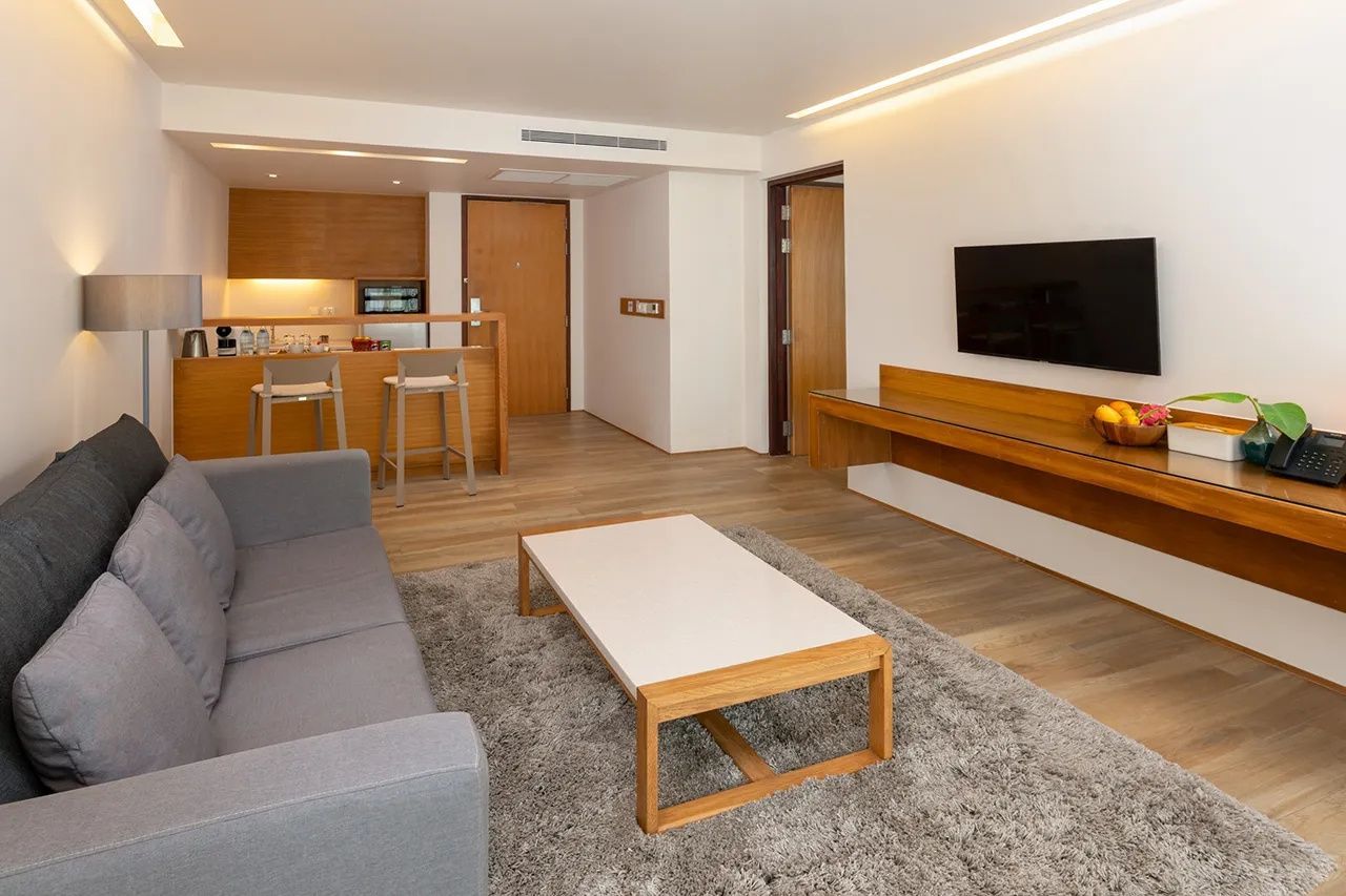 Offener Wohnbereich einer Suite mit Couch, Couchtisch, Wandfernseher und Küchenzeile.