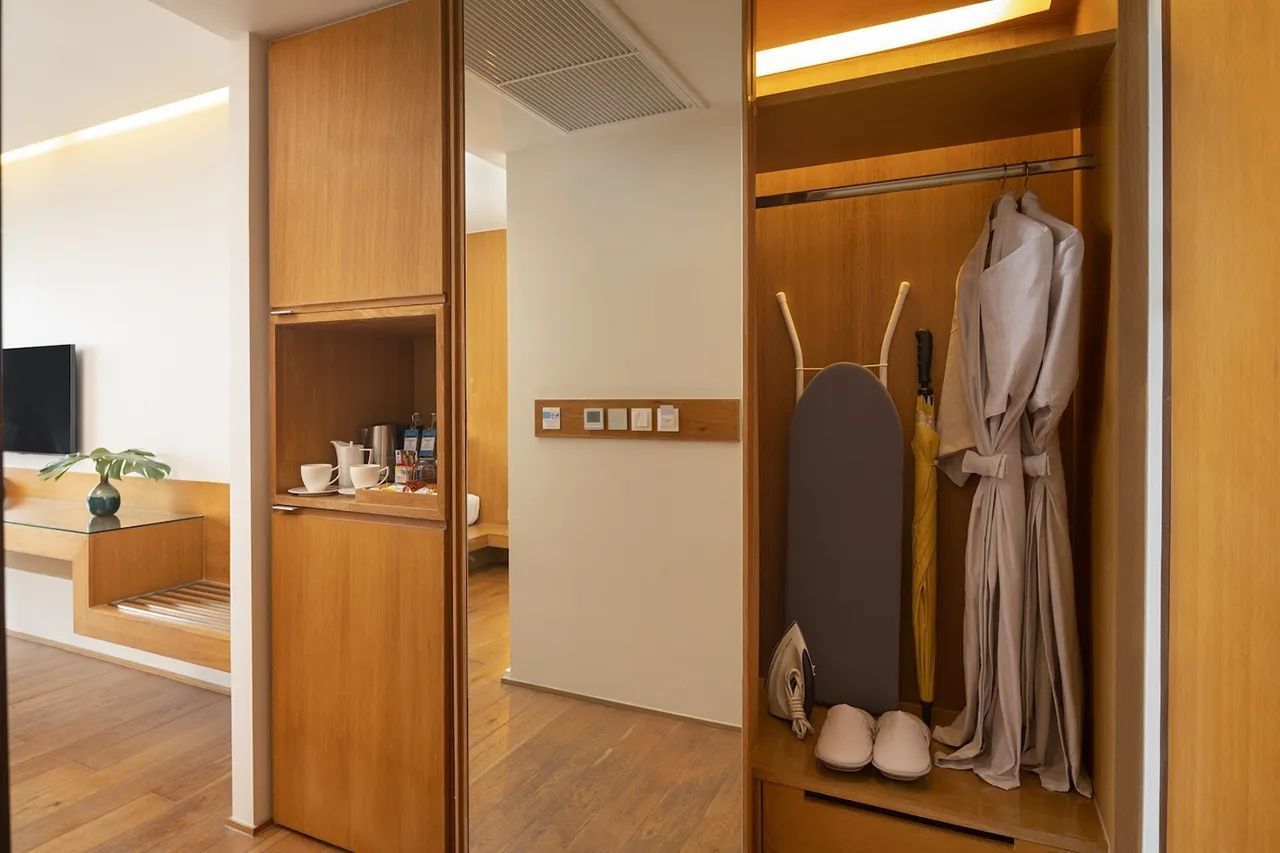 Eingangsbereich des Zimmers mit Holzschrank, Bademantel, Bügelbrett und Minibar.