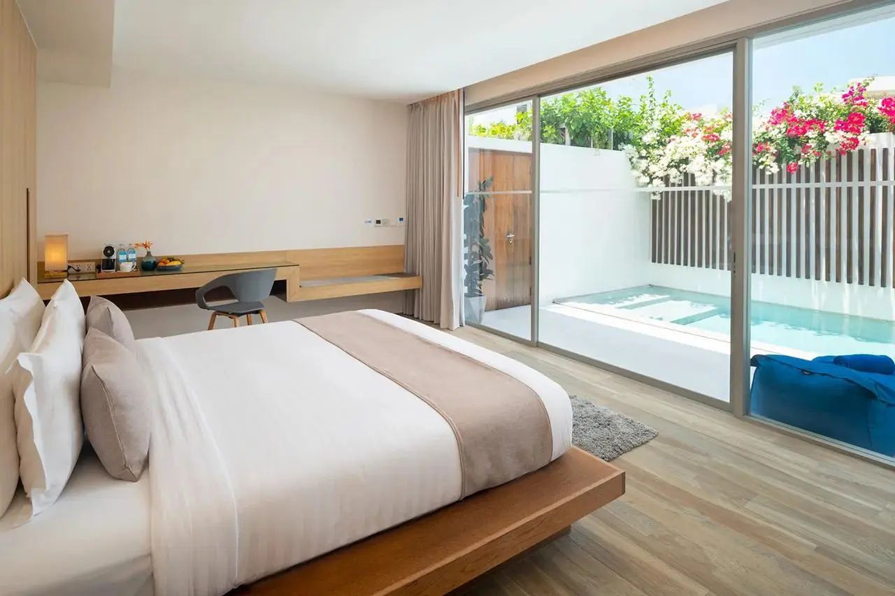 Hell eingerichtetes Hotelzimmer mit Holzboden und Blick durch Glasschiebetüren zum Außenpool.