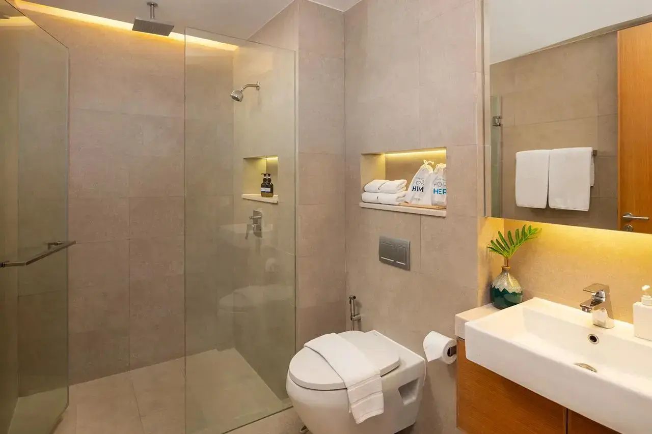 Badezimmer mit bodengleicher Glasdusche, Toilette sowie beleuchteter Ablagenische.