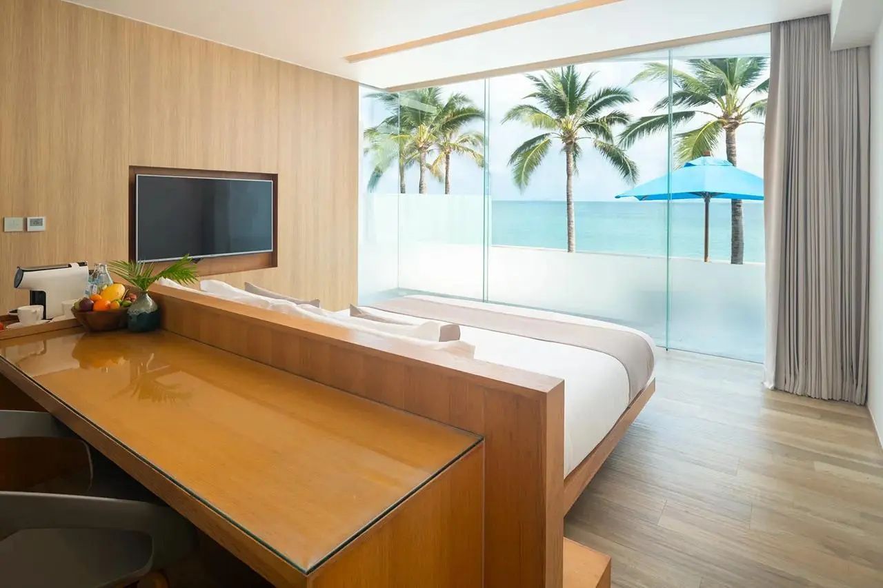 Helles Schlafzimmer mit Holzschreibtisch, Doppelbett und Panoramablick auf das Meer.