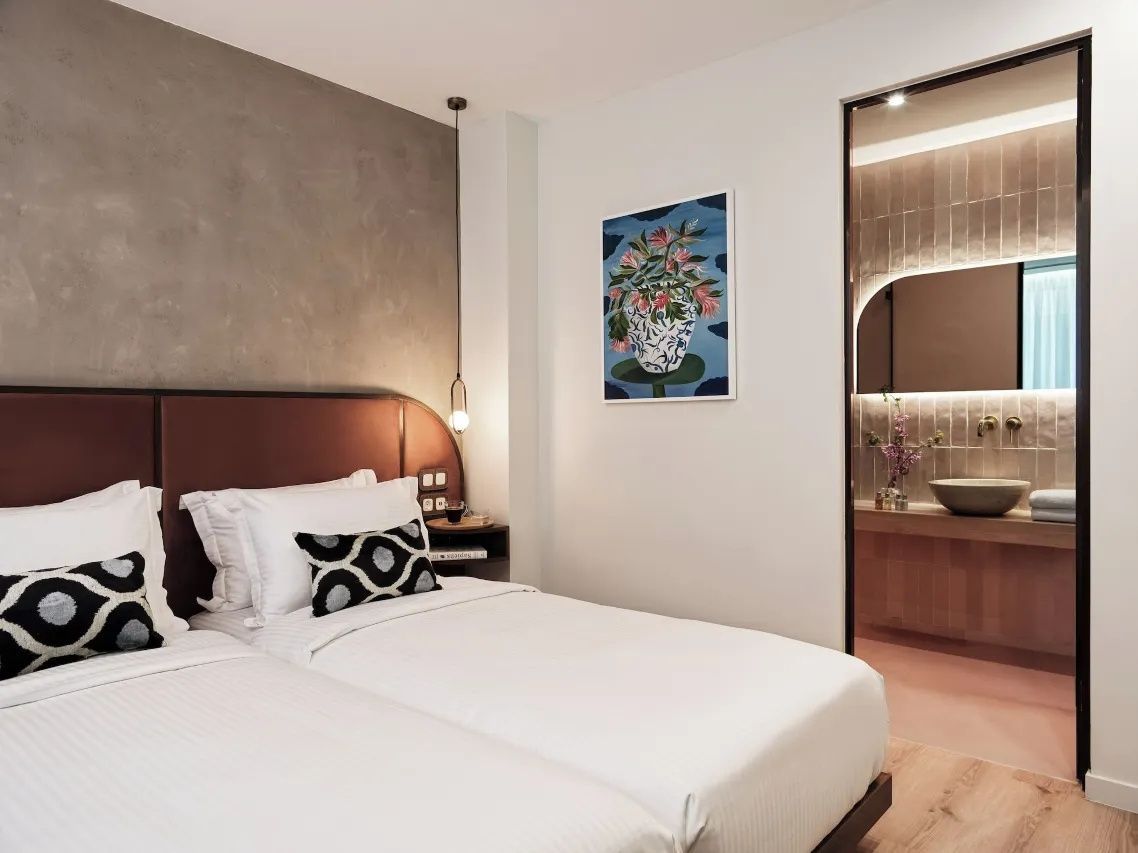 Hotelzimmer mit zwei nebeneinander stehenden Betten, Wandbild und Blick ins angrenzende Badezimmer.