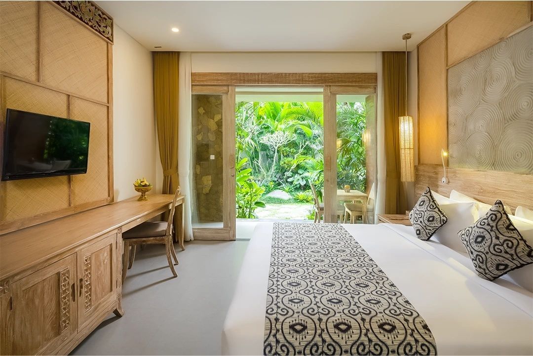 Helles Hotelzimmer mit Doppelbett, Holzschreibtisch und Blick auf den grünen Garten.
