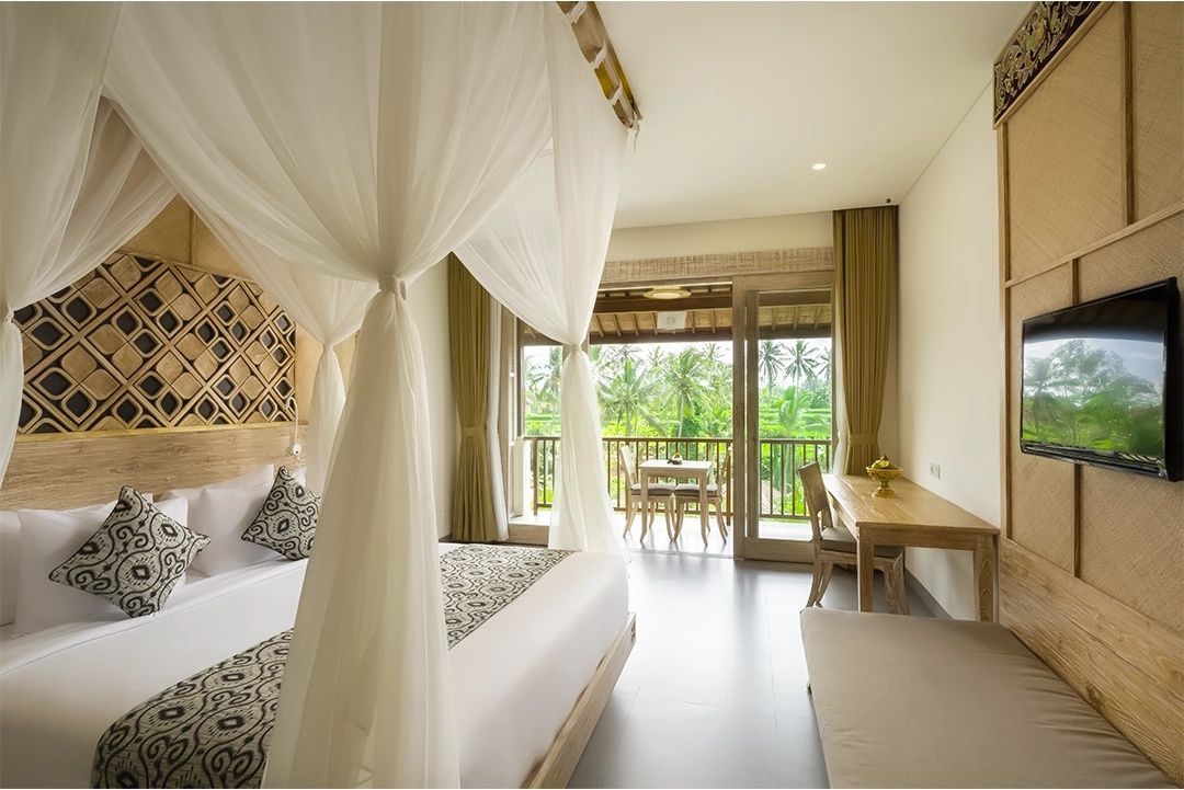 Helles Hotelzimmer mit großem Himmelbett, Holzmöbeln und Blick auf einen grünen Balkon.