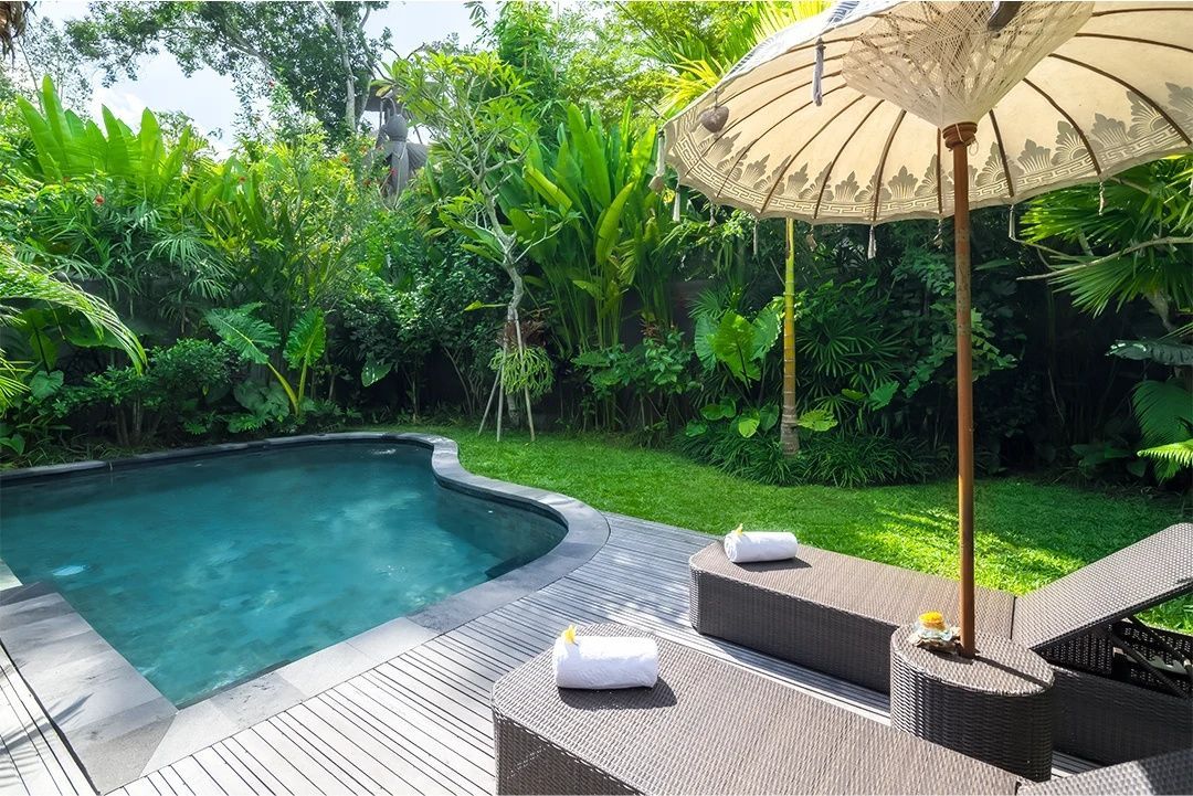 Pool mit Holzdeck, zwei Sonnenliegen unter einem traditionellen Sonnenschirm