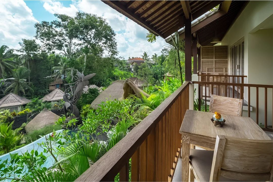 Blick von einem Holzbalkon auf die umliegende tropische Vegetation und Resort-Dächer.