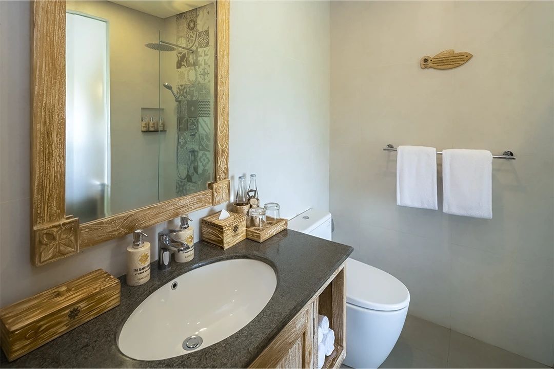 Badezimmer mit Waschbecken auf Holzunterschrank, Spiegel, Toilette und Dusche.