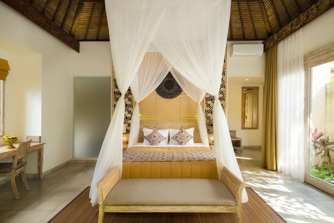 Großes Doppelbett mit weißem Moskitonetz und Holzbank im Schlafbereich einer Villa