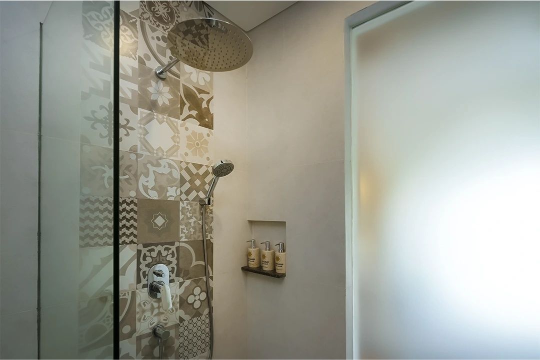 Dusche mit Regenduschkopf, Handbrause und gemusterten Fliesen an der Wand.