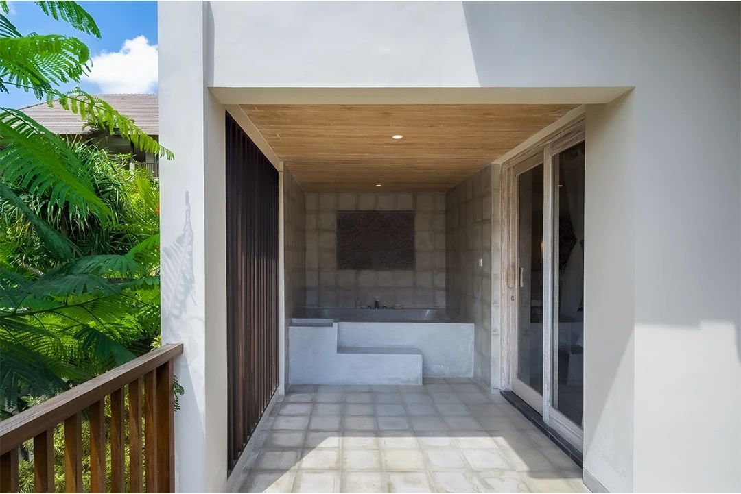 Überdachter Außenbereich einer Villa mit eingelassener Badewanne und grauem Fliesenboden.