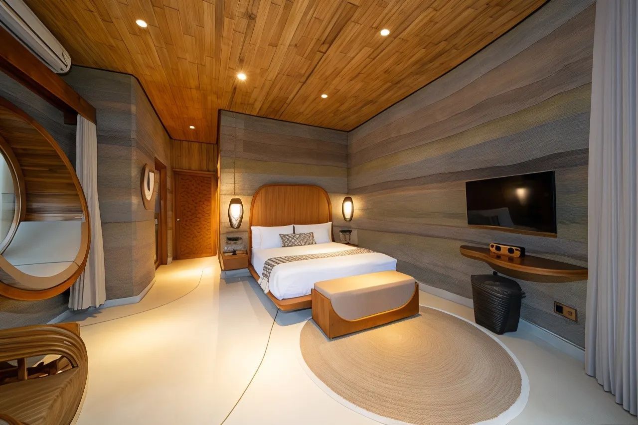 Geräumiges Hotelzimmer mit Holzdoppelbett, Fernseher und Wänden in Stampflehm-Optik.