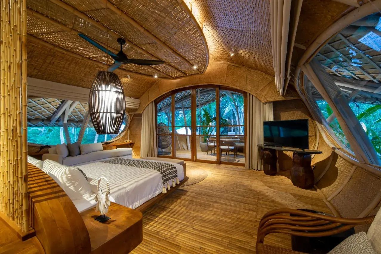 Schlafzimmer mit Bambusdecke, Fernseher und Blick durch große Glas-Schiebetüren auf die Terrasse.