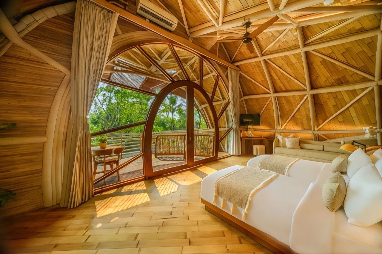 Schlafzimmer mit großer gebogener Glastür, die auf den Balkon ins Grüne führt.