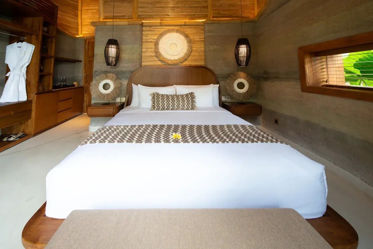Doppelbett mit weißer Bettwäsche und Wanddekoration aus Naturmaterialien in einer Bambusvilla.