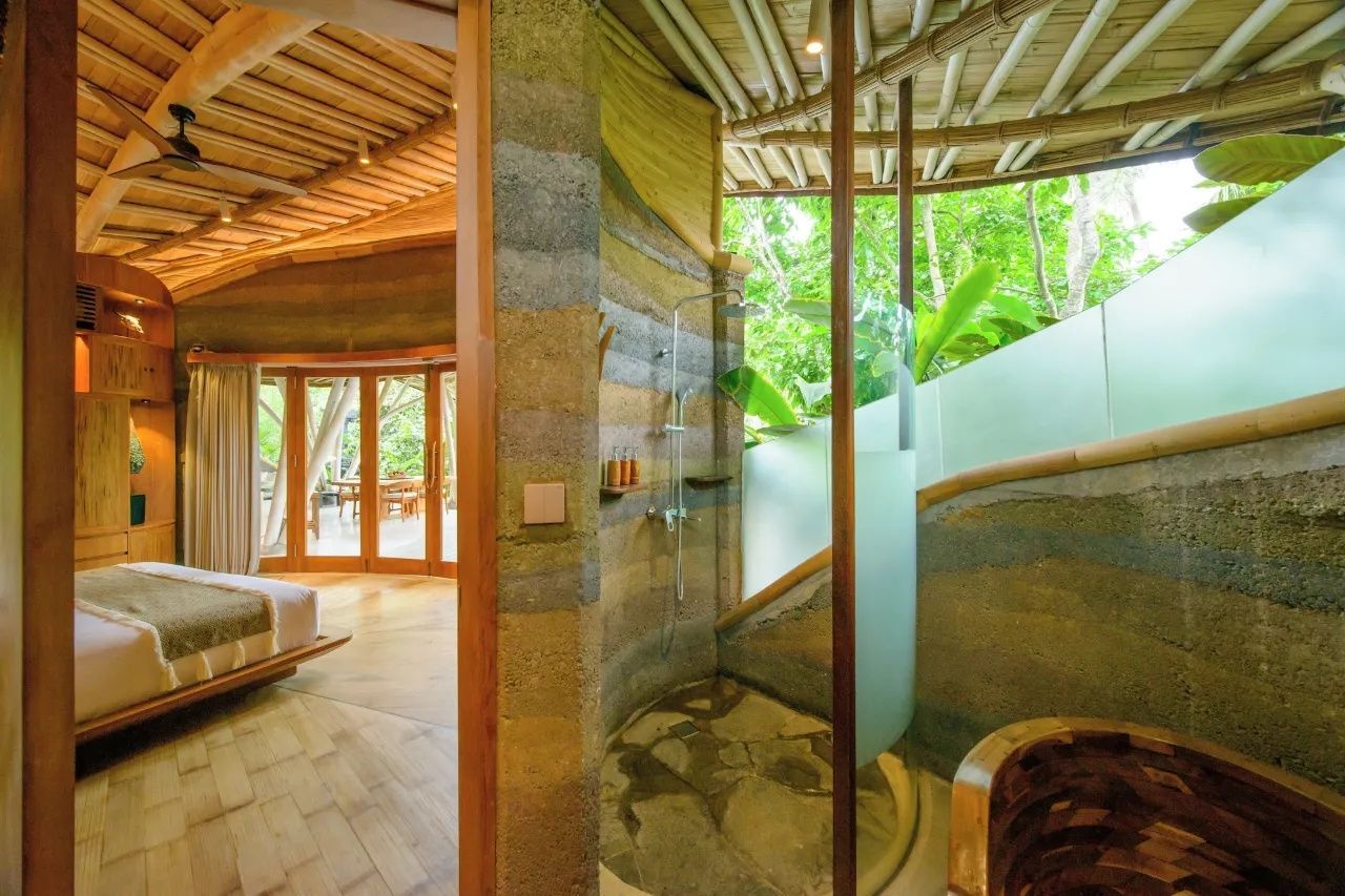 Badebereich mit Dusche hinter einer Glasscheibe und Sicht auf grüne Pflanzen im Außenbereich.