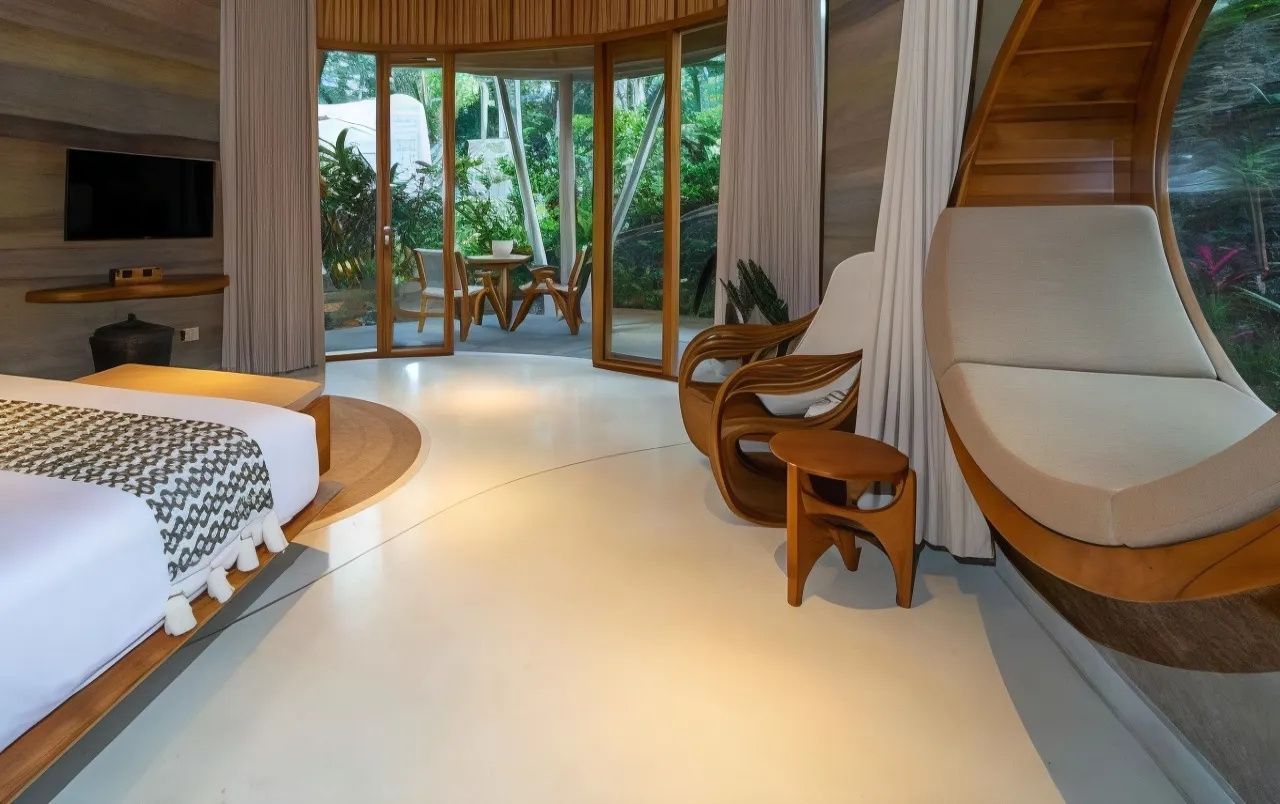 Sitzbereich im Zimmer mit geschwungenen Holzsesseln und Blick auf die Terrasse durch Glastüren.