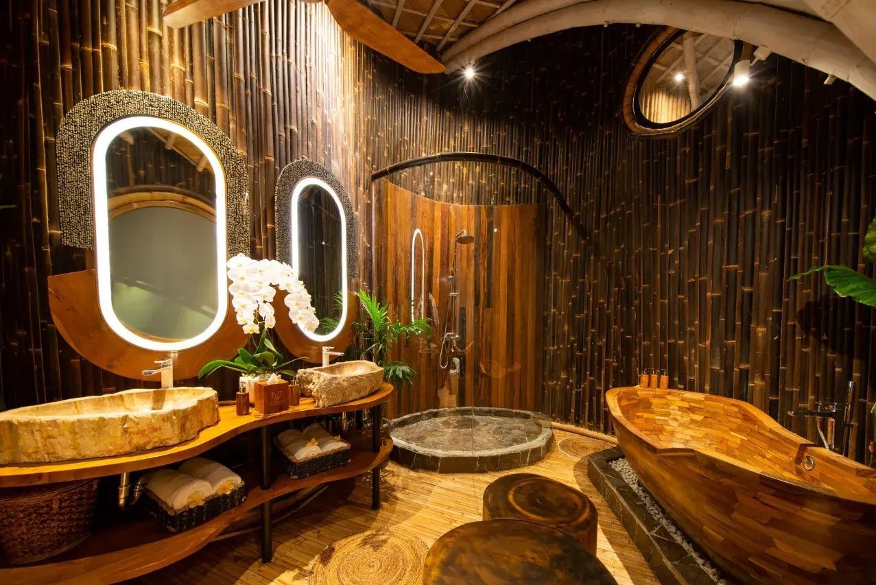 Badezimmer mit Wänden aus dunklem Bambus, beleuchteten Spiegeln, Steinwaschbecken und Holzwanne.