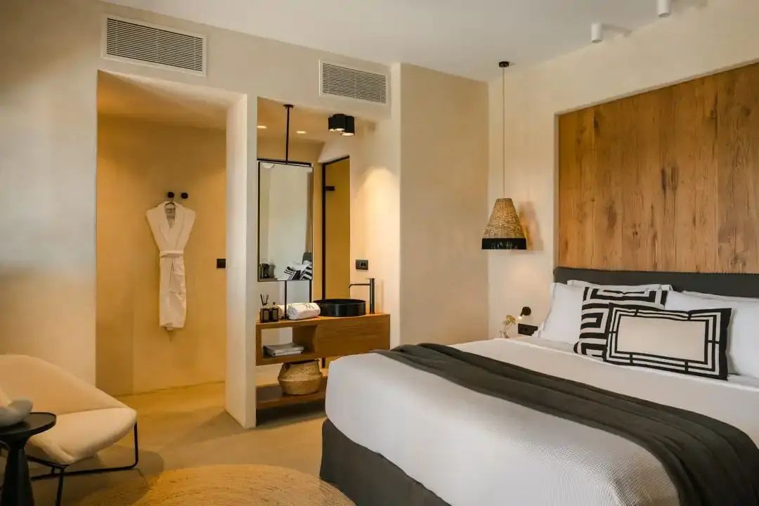 Helles Hotelzimmer mit Doppelbett, Holzkopfteil und offenem Waschbereich mit Holzwaschtisch.