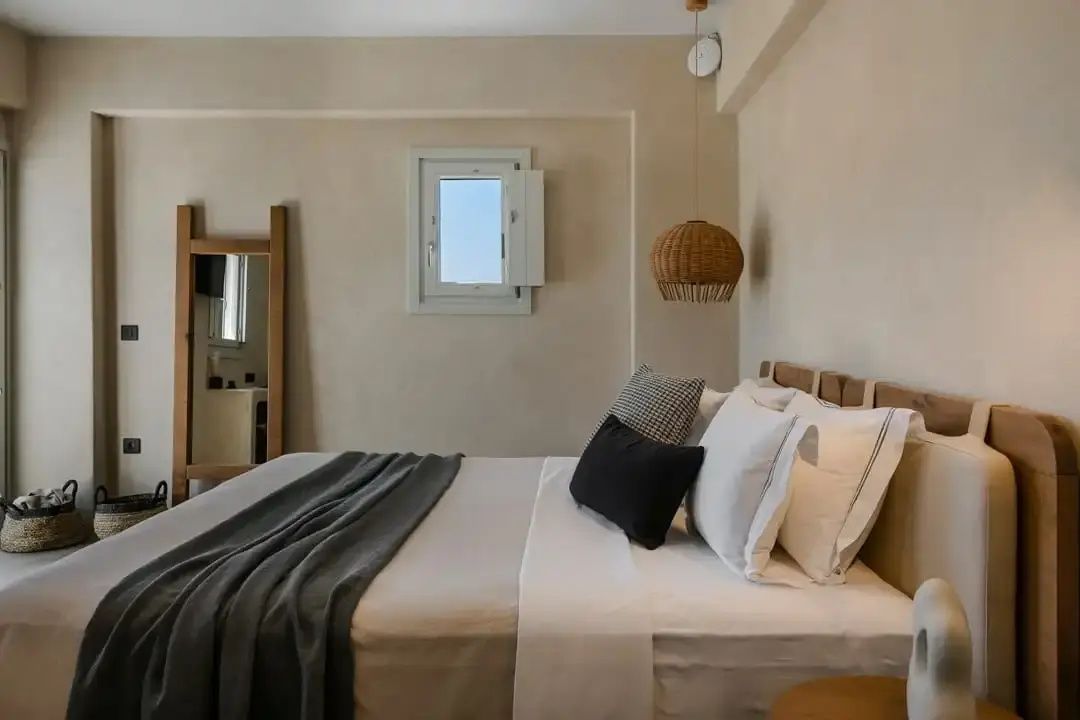 Helles Hotelzimmer mit Doppelbett, beigen Wänden und Flechtlampe.