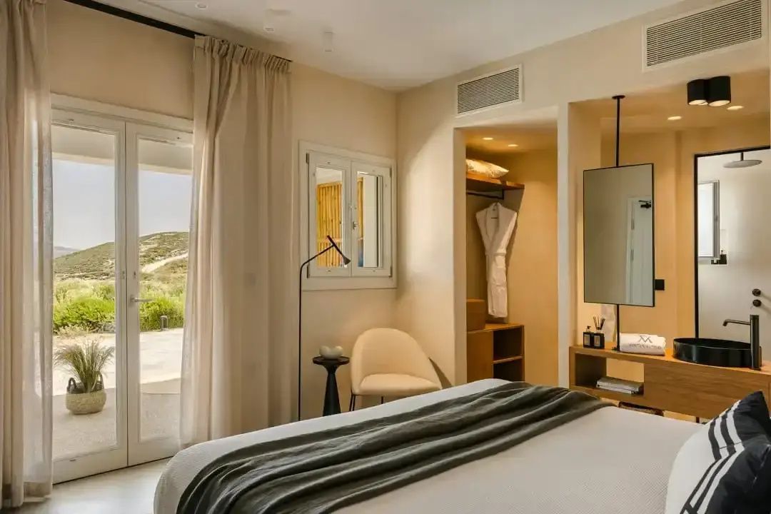 Hotelzimmer mit Doppelbett, Sessel, hellen Vorhängen und Blick durch die Balkontür auf die Landschaft.