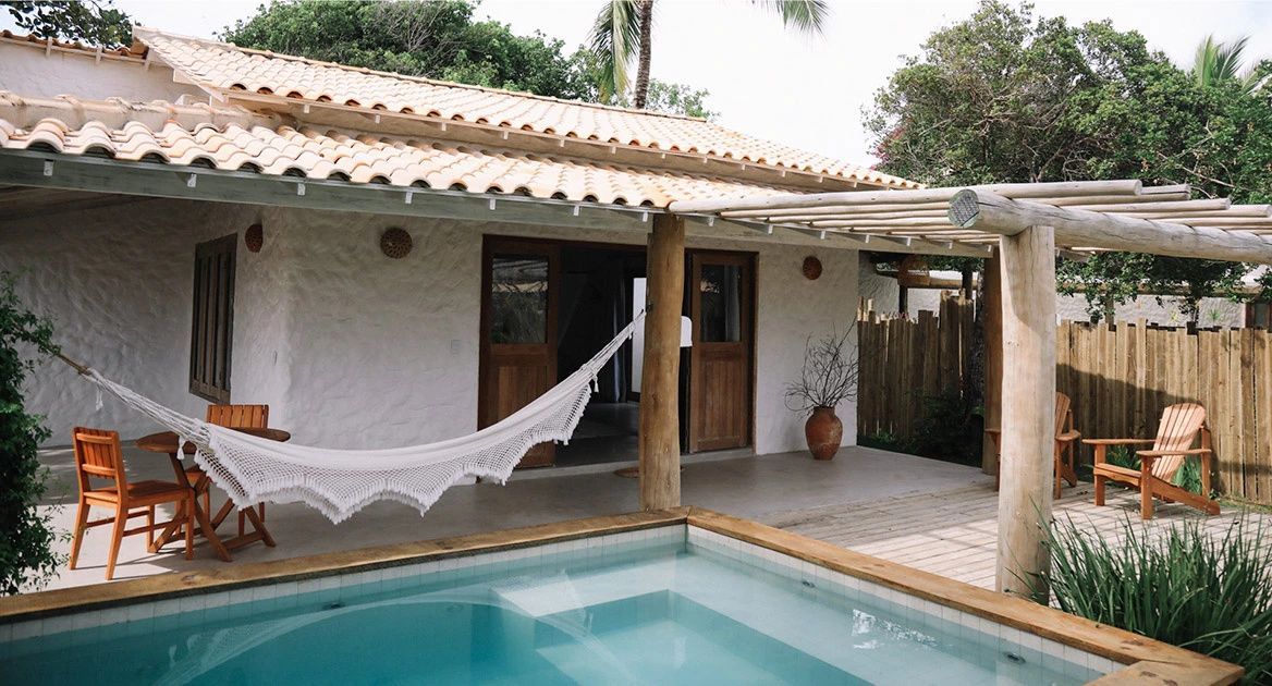 Außenansicht eines Bungalows mit überdachter Terrasse, Hängematte und Pool.