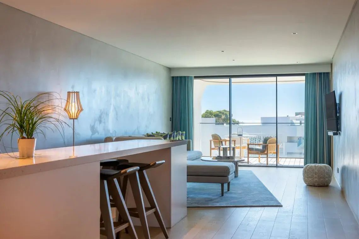 Modernes Wohnzimmer einer Suite mit Tresen, Barhockern, Sofa und Zugang zum Balkon.