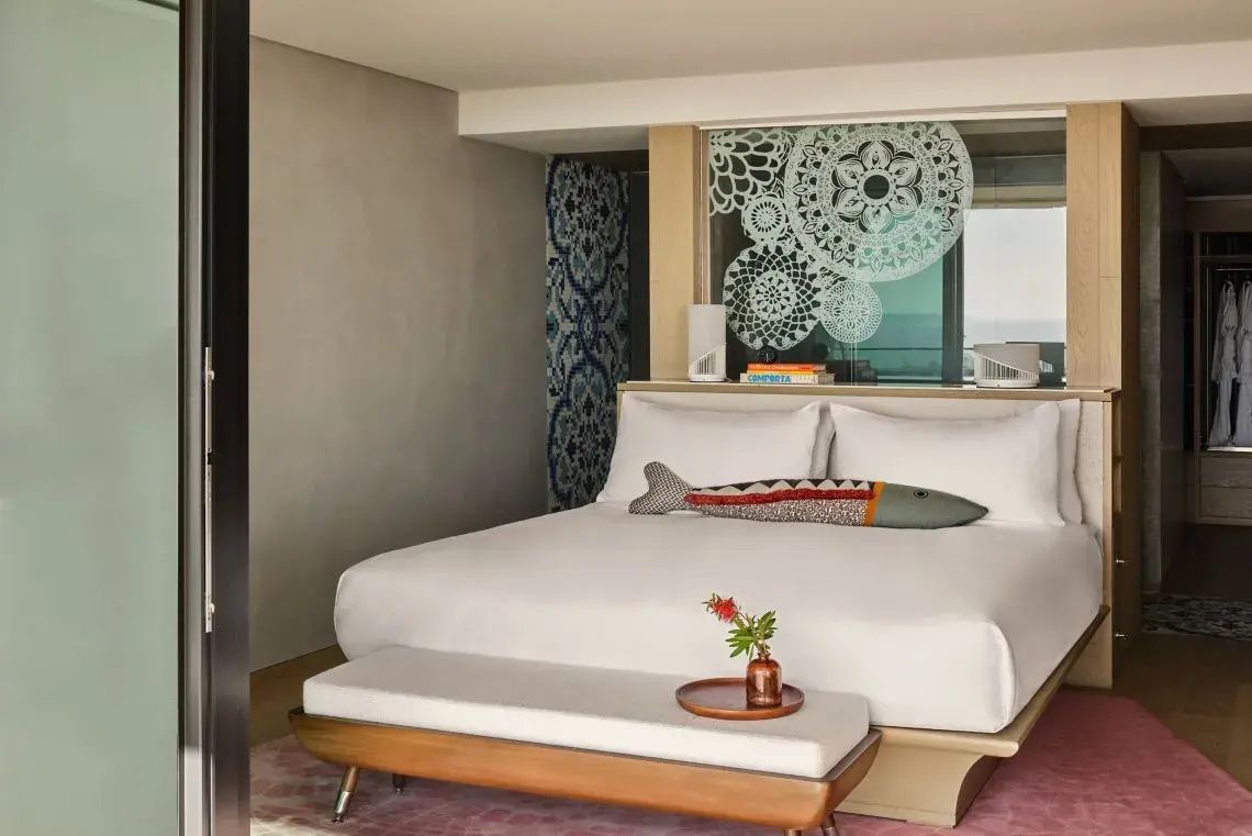 Doppelbett mit weißer Bettwäsche und fischförmigem Kissen in einem modern eingerichteten Hotelzimmer.