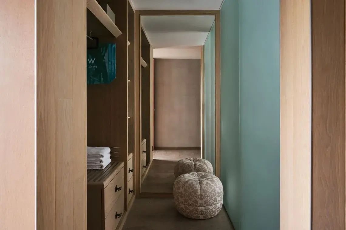 Ankleidebereich im Hotelzimmer mit Holzschrank, Spiegel und zwei Hockern.