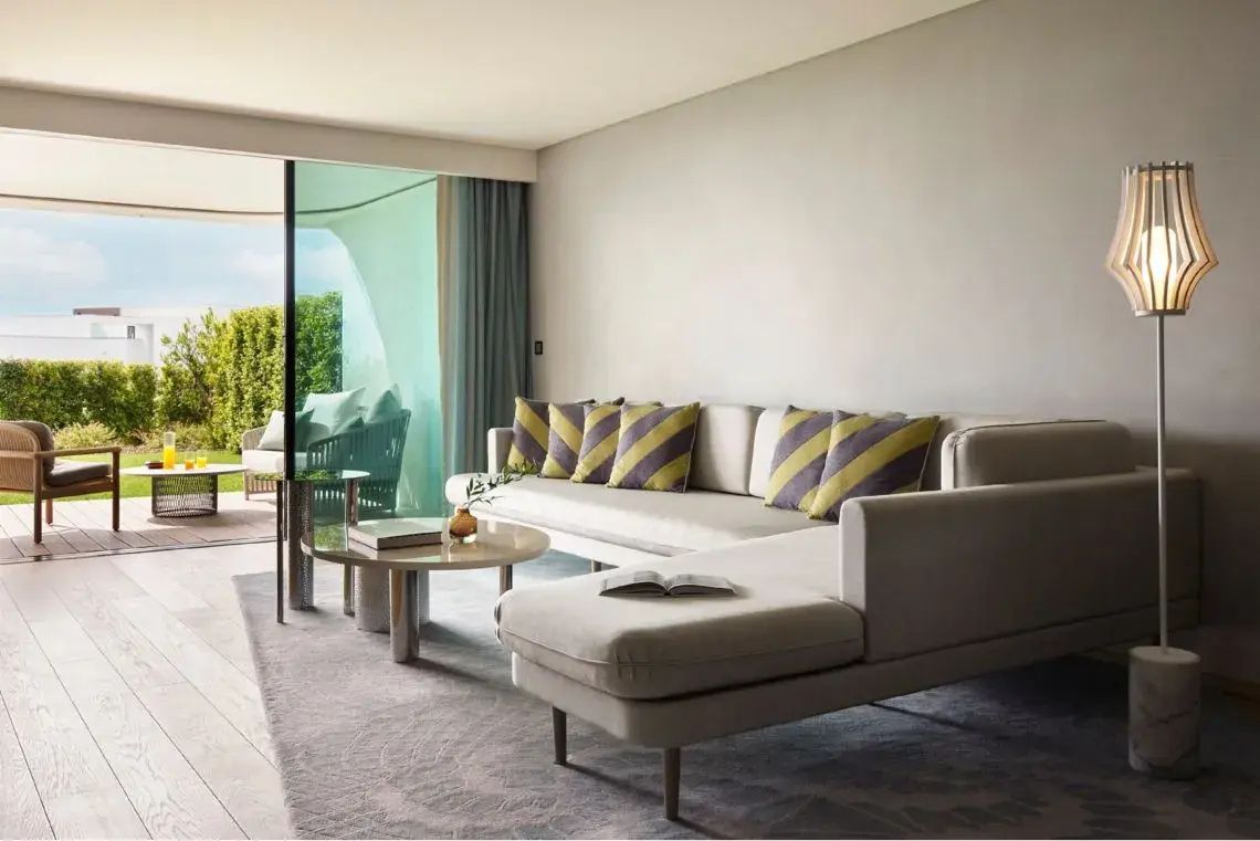 Wohnbereich einer Suite mit hellem Ecksofa, Kissen und Zugang zur Terrasse.