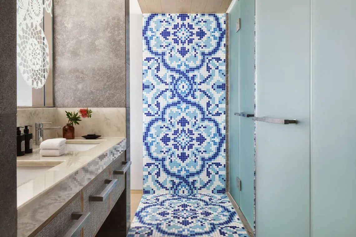 Badezimmer mit blau gemusterten Mosaikfliesen an Wand und Boden sowie einem Waschtisch.