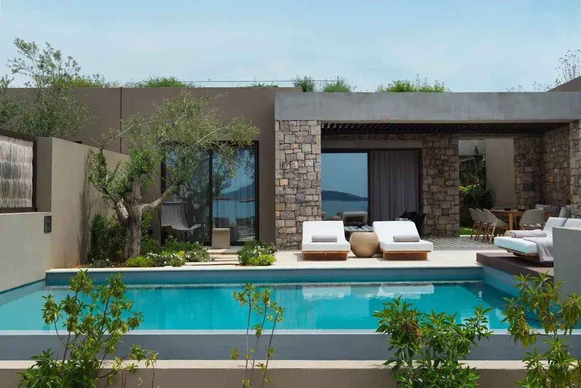 Außenansicht der Villa mit privatem Pool, zwei Sonnenliegen und Bepflanzung im Vordergrund.