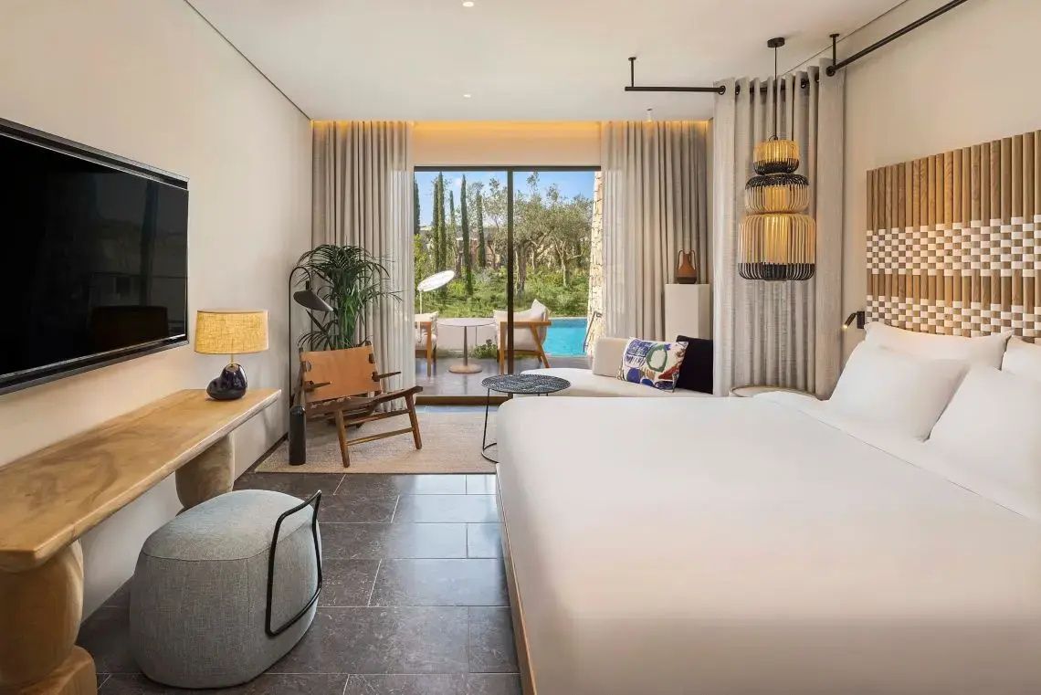 Helles Hotelzimmer mit Doppelbett, Sitzbereich und Zugang zur eigenen Terrasse mit Pool.