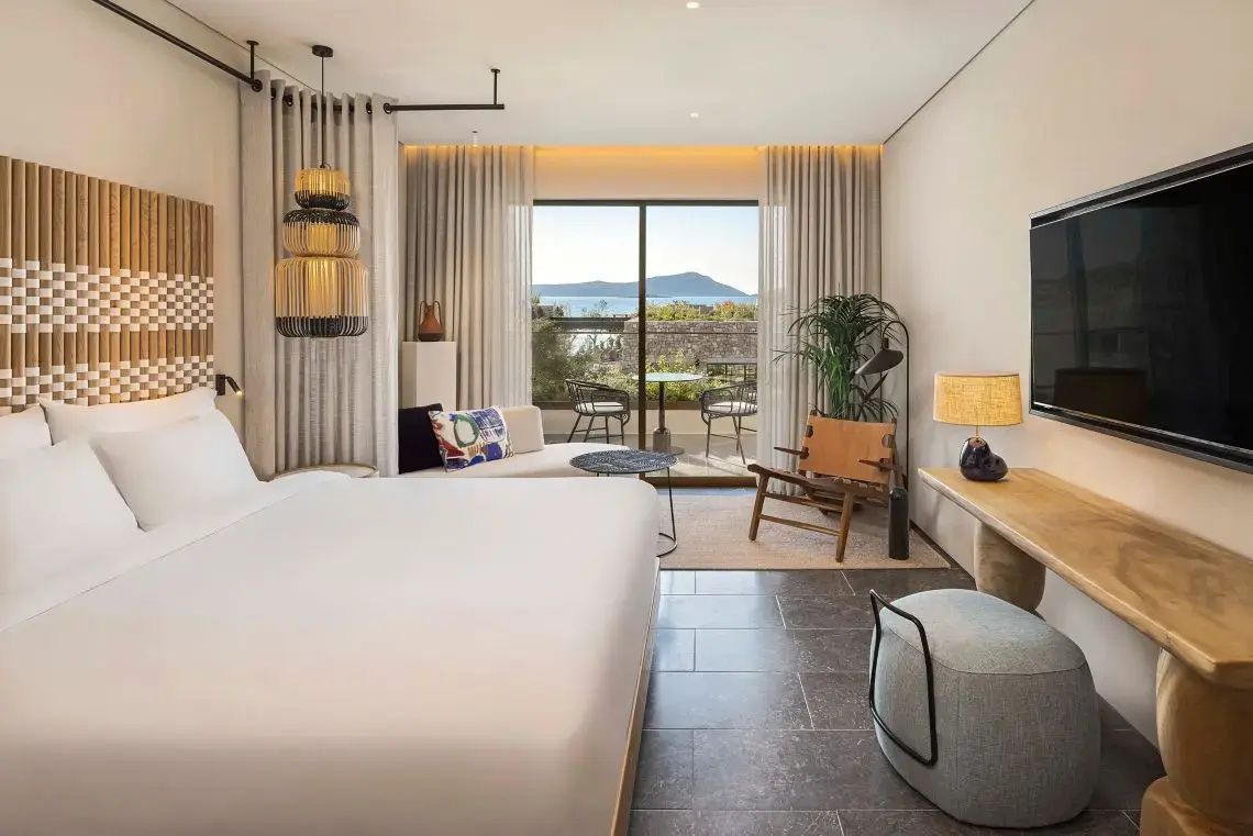 Modernes Hotelzimmer mit Doppelbett, Sitzbereich und Balkon mit Blick auf das Meer.