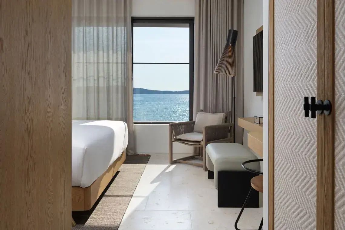 Sitzbereich im Zimmer mit Sessel, Polsterhocker und Ausblick auf das ruhige Meer.