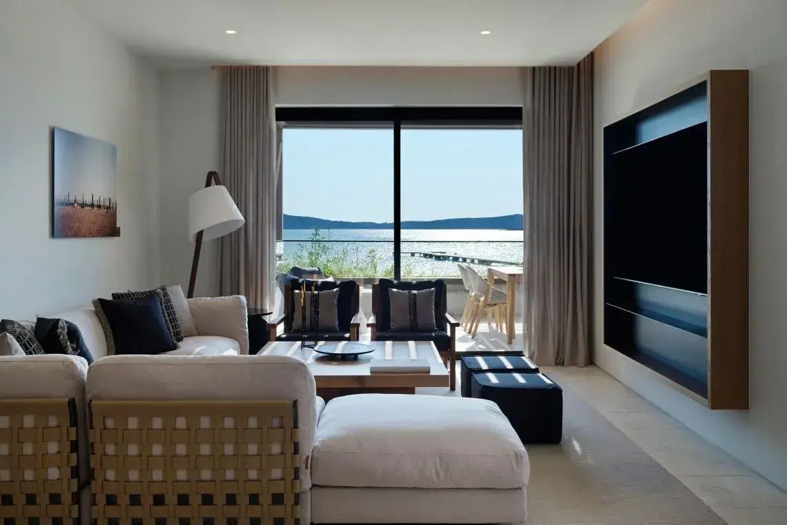 Wohnbereich einer Suite mit hellen Sesseln, Sofa und großen Fenstern zum Meer.
