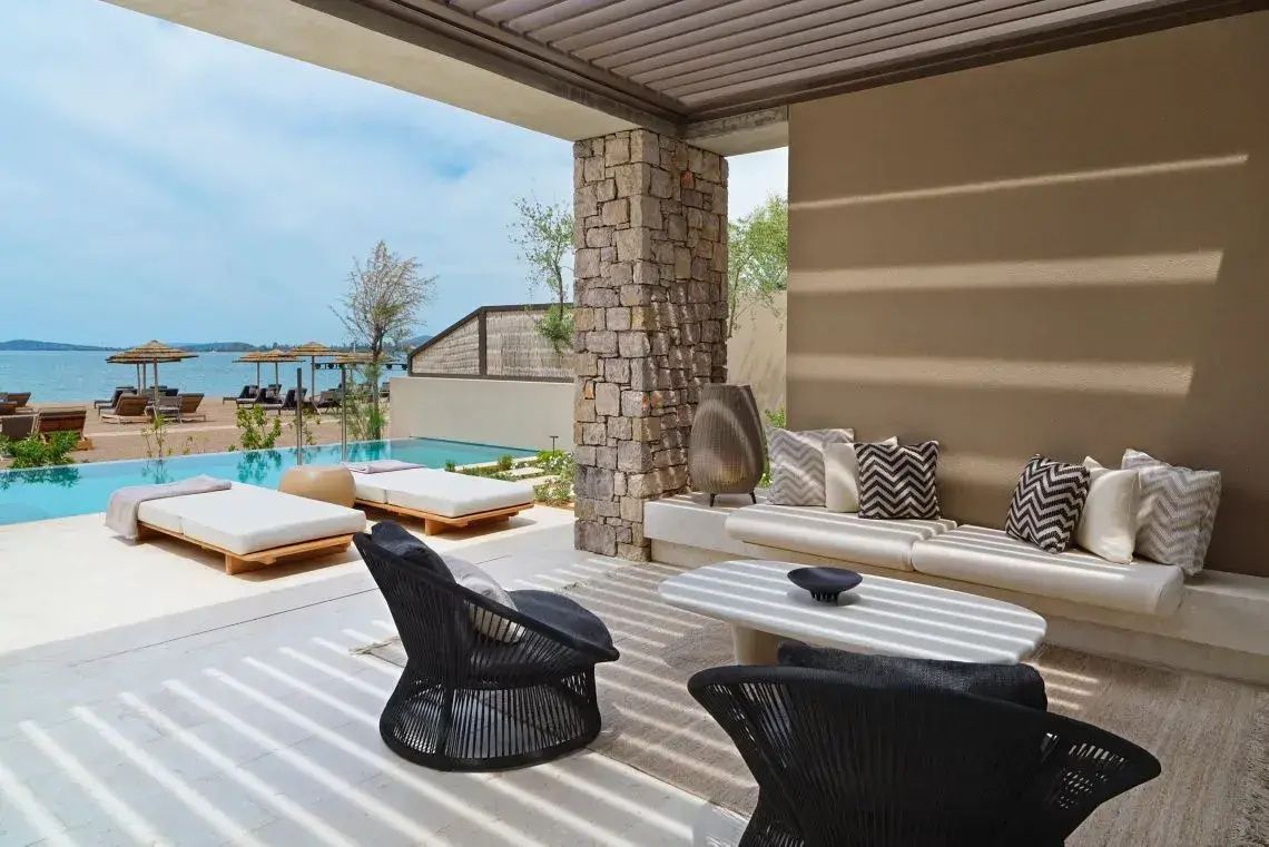 Überdachte Terrasse mit Sitzgelegenheiten, privatem Pool und Blick auf das Meer im Hintergrund.