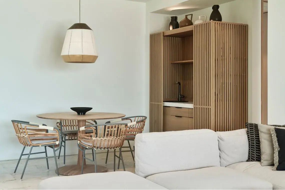 Esstisch mit Stühlen aus Holz und Flechtwerk neben einer Bar im Wohnbereich einer Suite.