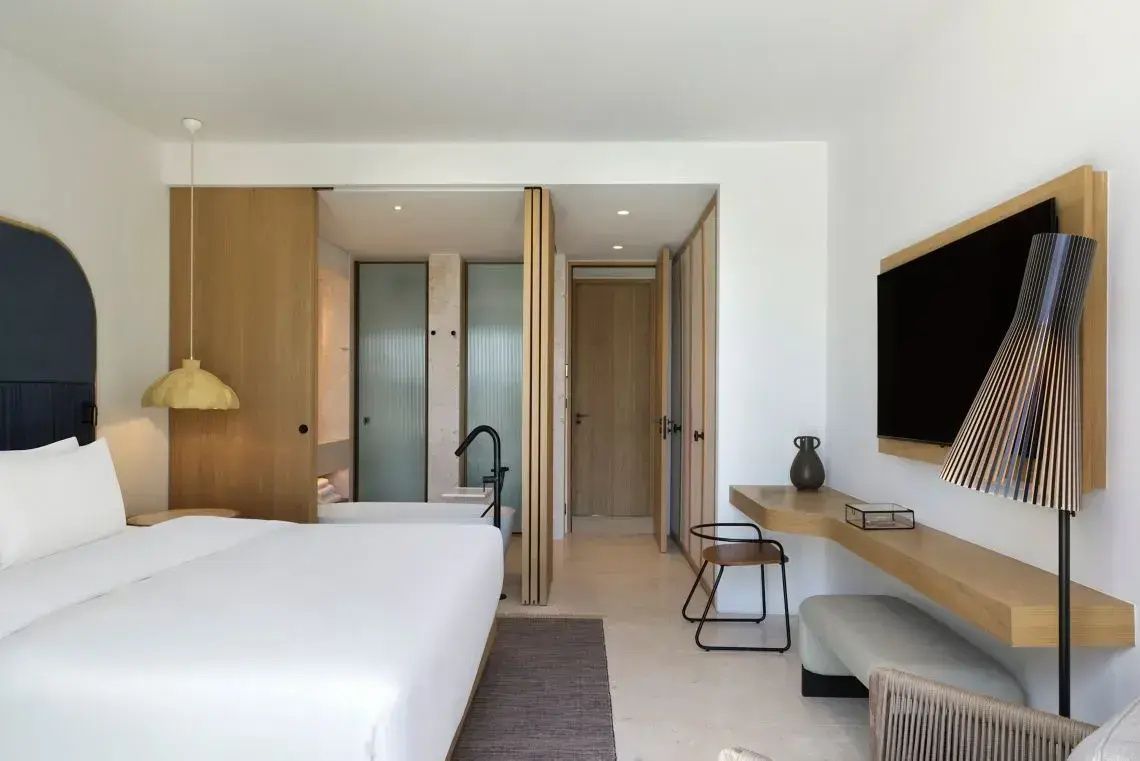 Modernes Hotelzimmer mit Doppelbett, Schreibtisch an der Wand und Zugang zum Badezimmer.