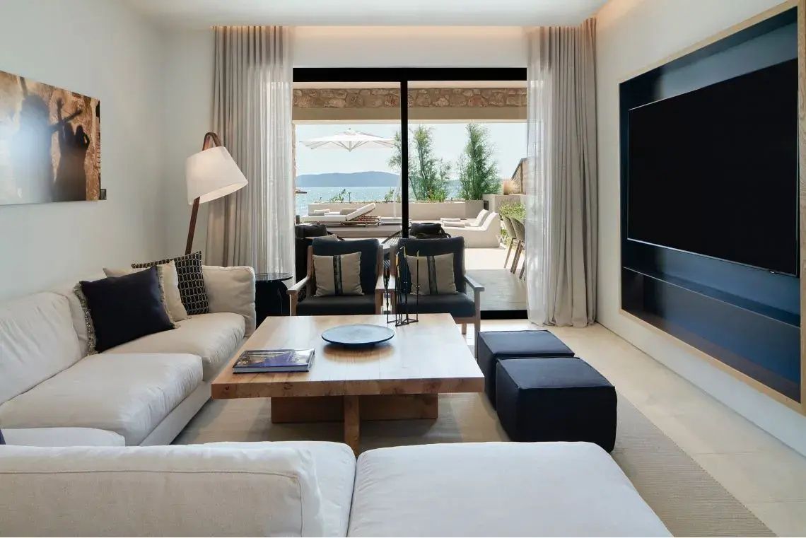 Heller Wohnbereich mit Sofas, Holztisch und Blick durch Schiebetüren auf Terrasse und Meer.