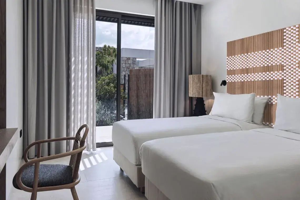 Modernes Zimmer mit zwei Einzelbetten, Holzstuhl und großem Fenster zum Garten.
