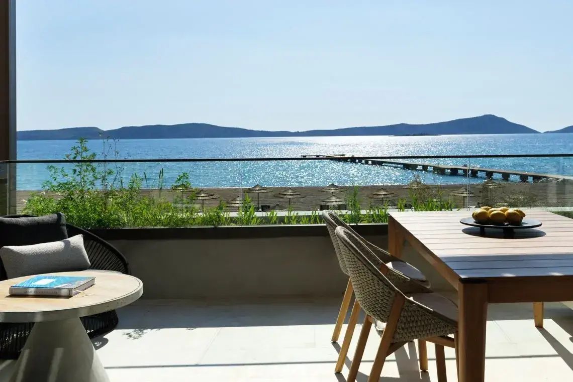 Aussicht von der Terrasse mit Holztisch und Stühlen auf das Meer und den Steg.
