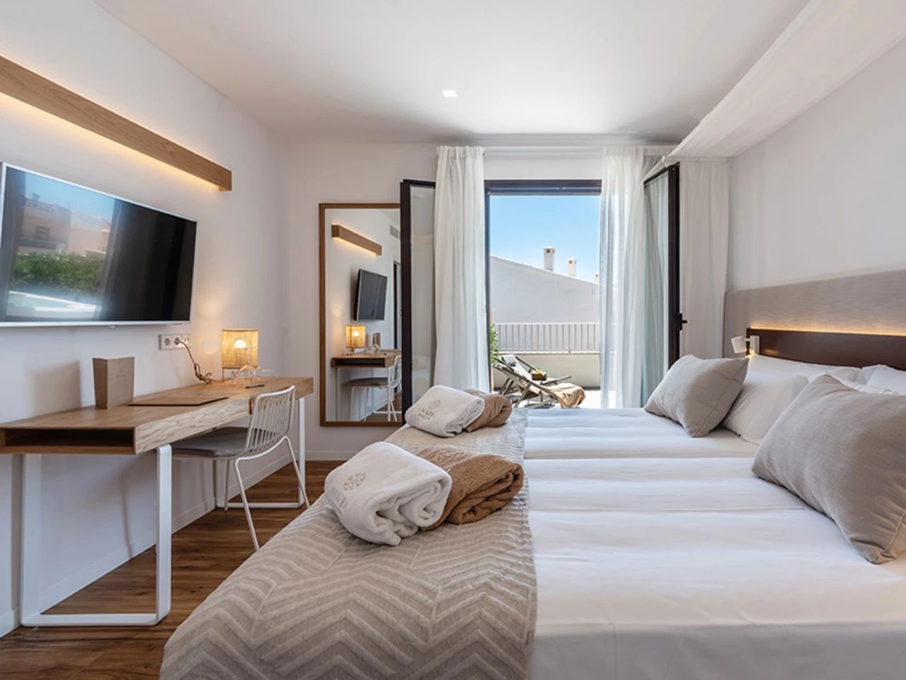 Helles Hotelzimmer mit Doppelbett, Schreibtisch und geöffneter Tür zur sonnigen Terrasse.