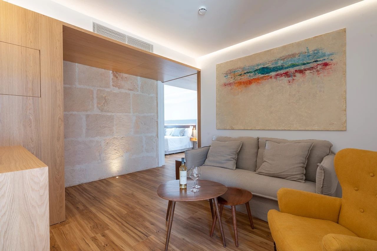 Wohnbereich mit beigefarbenem Sofa, Holzcouchtisch, Kunstwerk an der Wand und Natursteinwand.
