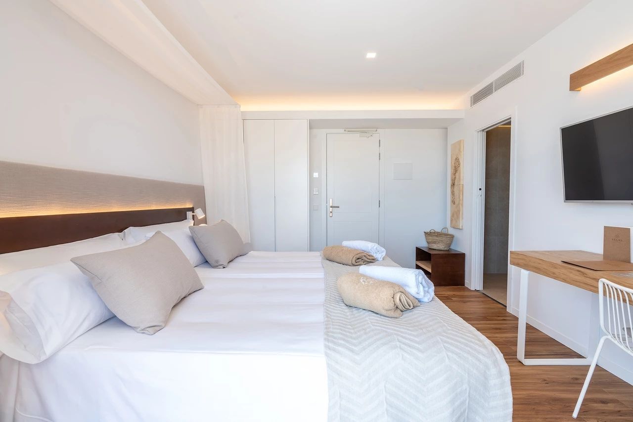 Schlicht gestaltetes Hotelzimmer mit großem Doppelbett, Parkettboden und weißem Einbauschrank.
