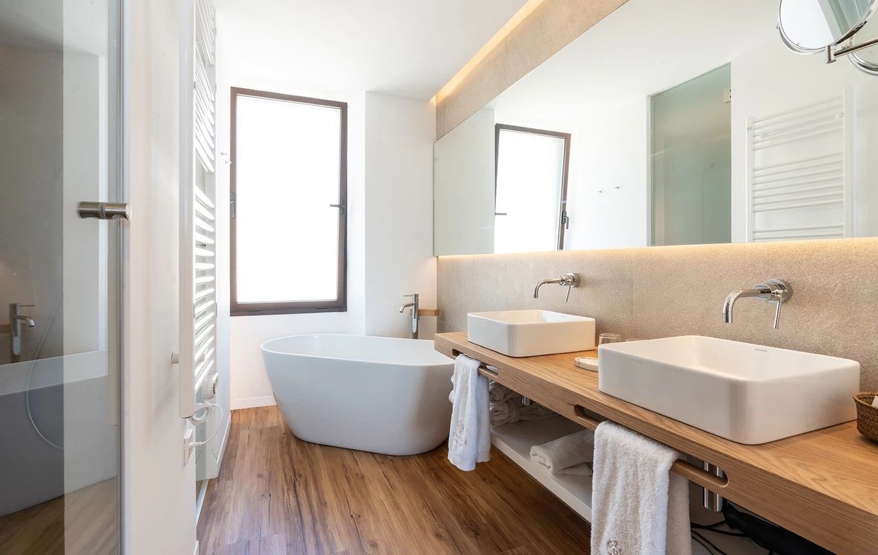 Badezimmer mit freistehender Badewanne, Doppelwaschtisch aus Holz und großem Spiegel.